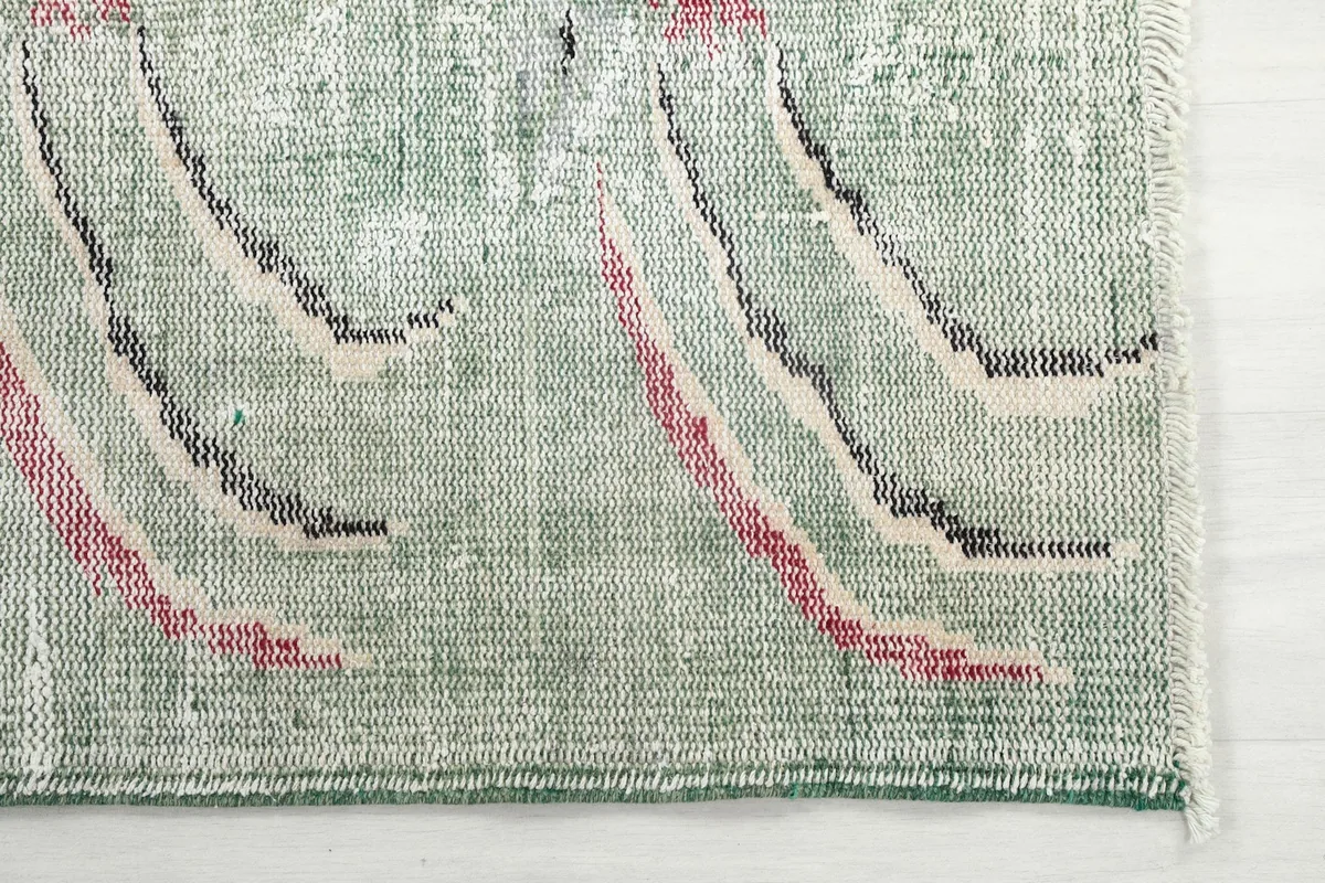 Detailed view of the rug's corner, showing the faded green pile and abstract rose, black, and beige patterns.
