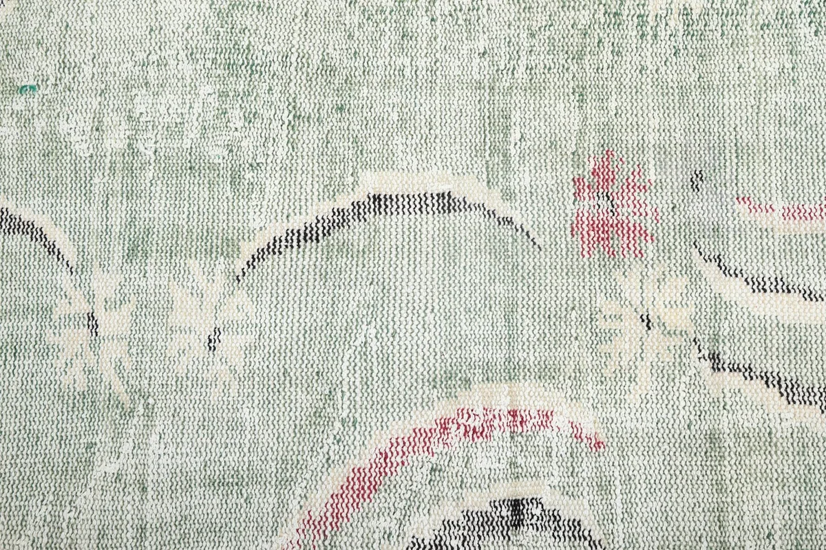 Close-up of the rug's surface, revealing the individual wool knots and the blend of faded green, rose, and black threads.