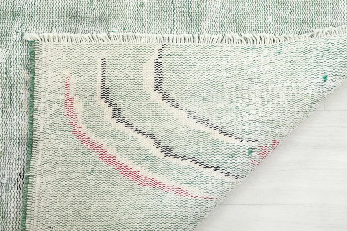 Underside of the hand-knotted rug with a corner folded, showing the cotton foundation and reverse of the pattern.