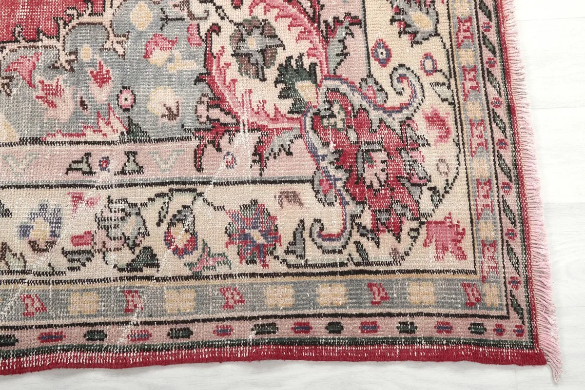 Detail of the rug's border design featuring floral and geometric motifs in beige, gray, and rose