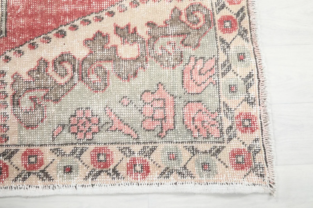 Close-up detail of the rug's corner showing floral and geometric motifs in rose, beige, and green.