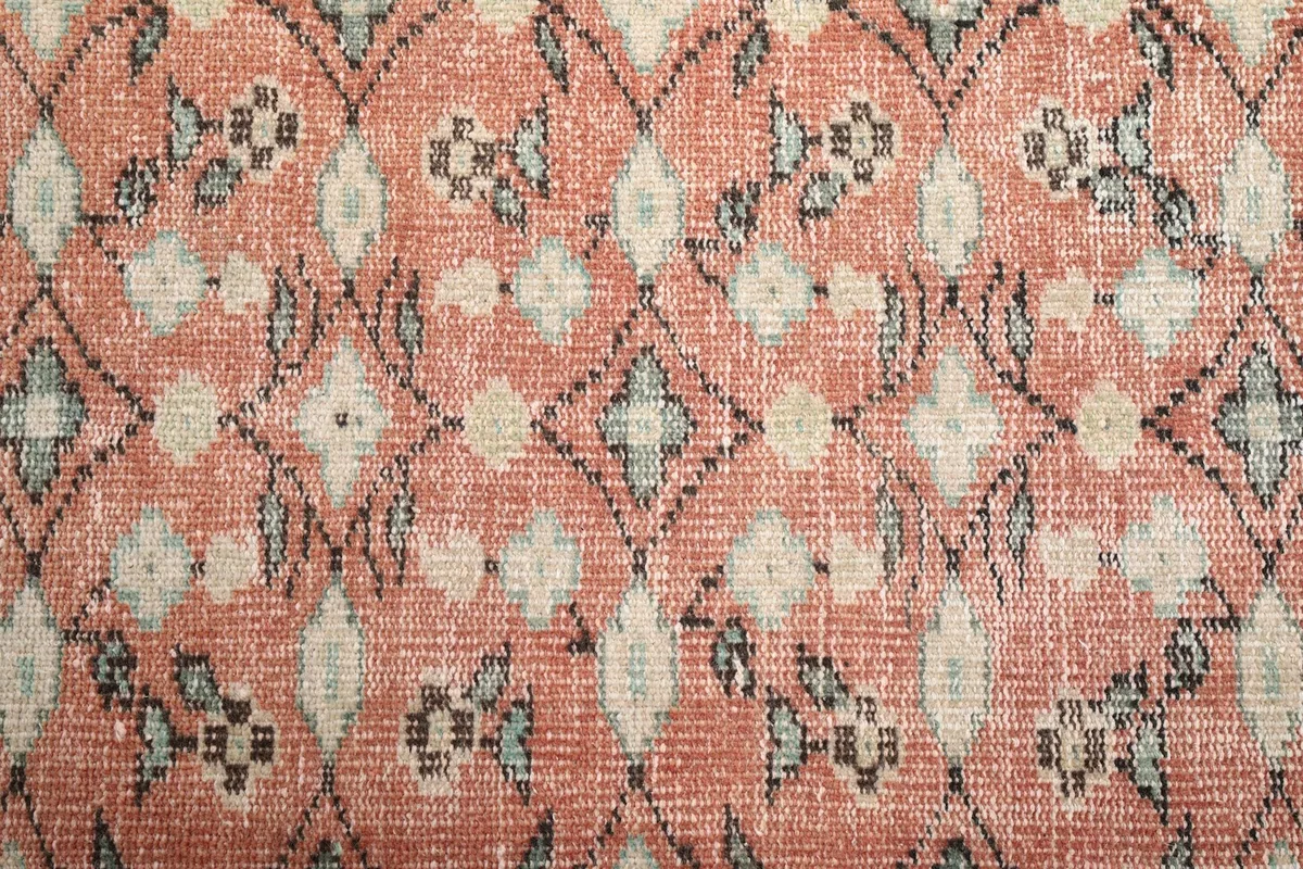 Close-up texture of the low wool pile showing the faded rose and geometric motifs.