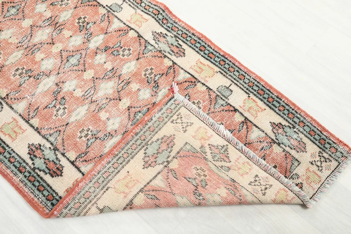 Corner of the rose runner rug folded over, revealing the intricate patterns and border design.