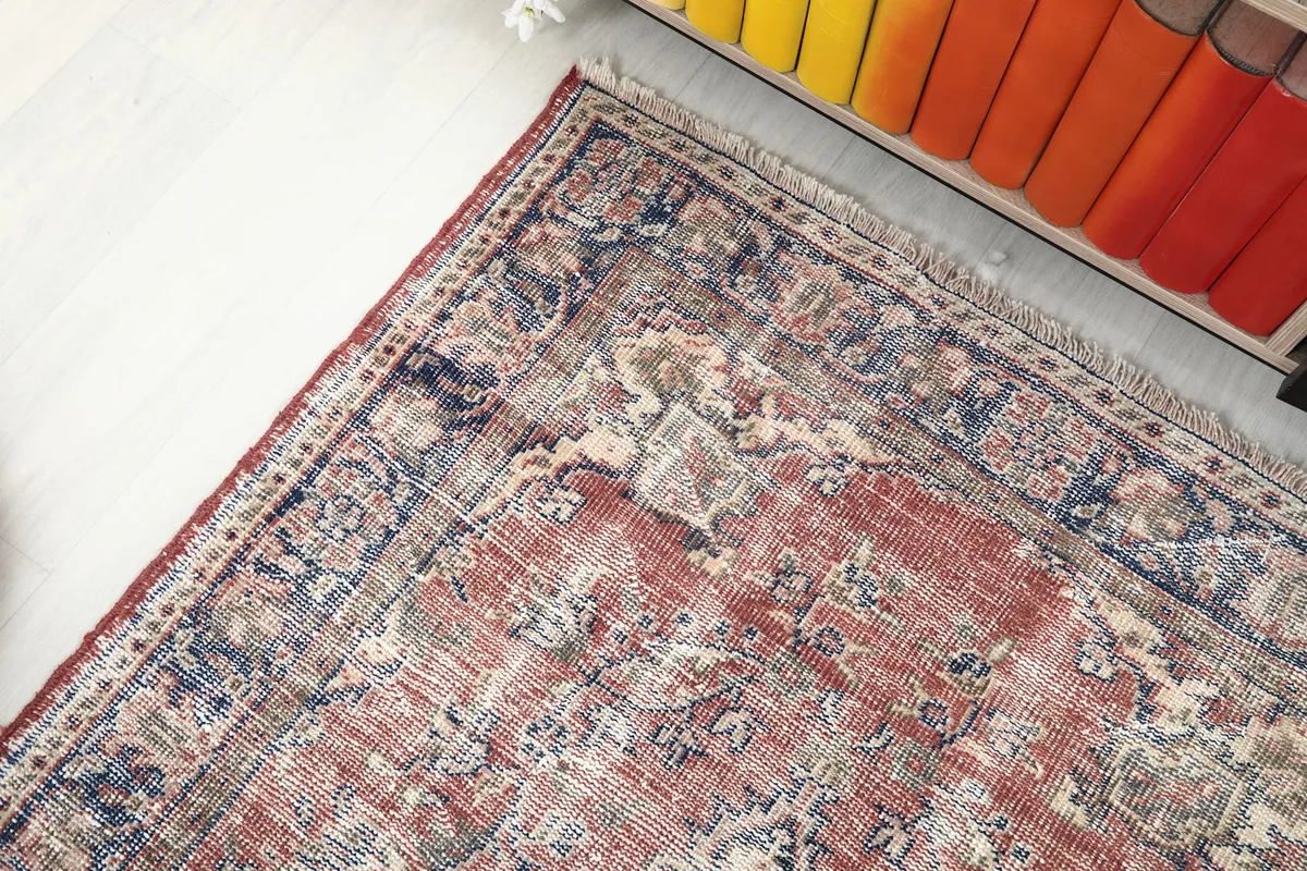 Corner view of the red vintage rug, showing the border details and distressed pile
