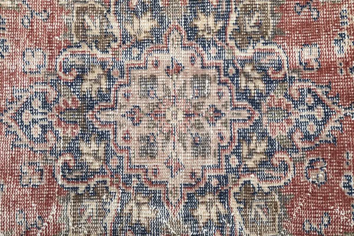 Close-up of the central medallion design, showing navy, beige, and cream motifs on a red background