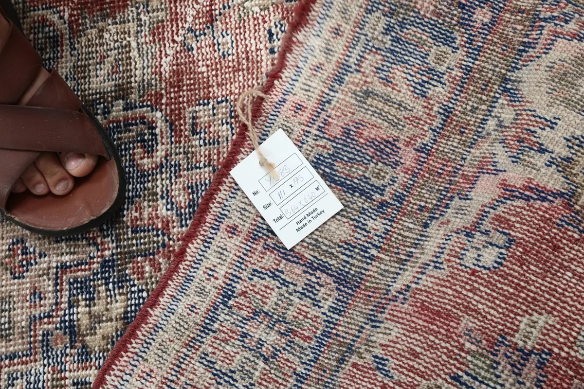 Detail showing a size tag on the vintage hand-knotted rug next to a foot