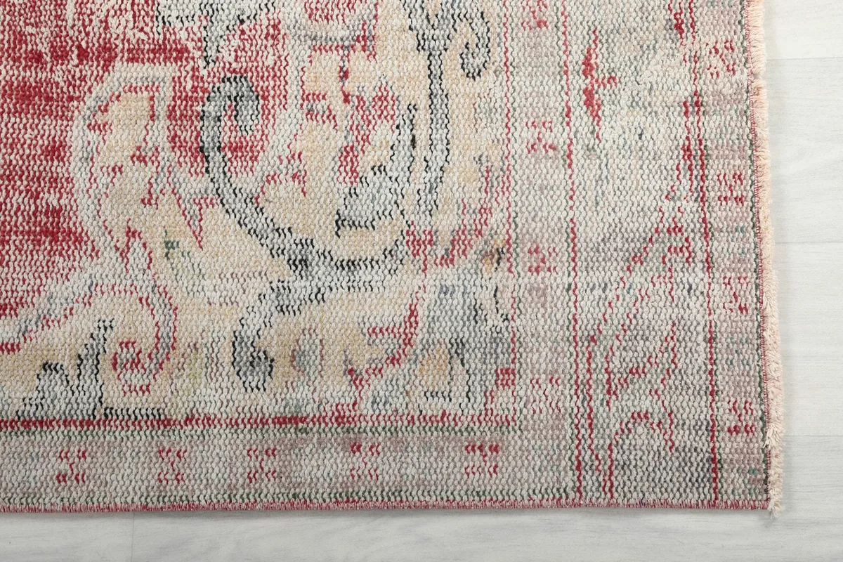 Detail of the rug's border, showing faded rose and cream motifs with a hint of blue.