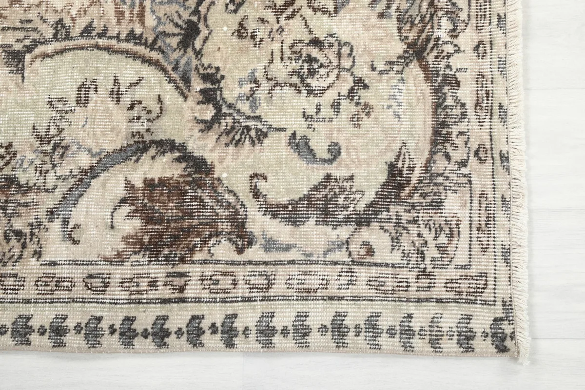 Detailed view of the rug's corner with faded gray and brown motifs and border