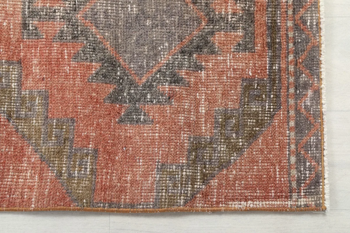Detailed shot of the hand-knotted wool pile and tribal geometric motif in rust and gray