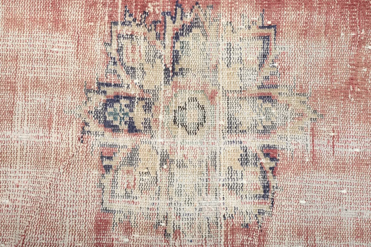 Close-up of a central geometric design on the rug, highlighting the worn wool pile and colors.