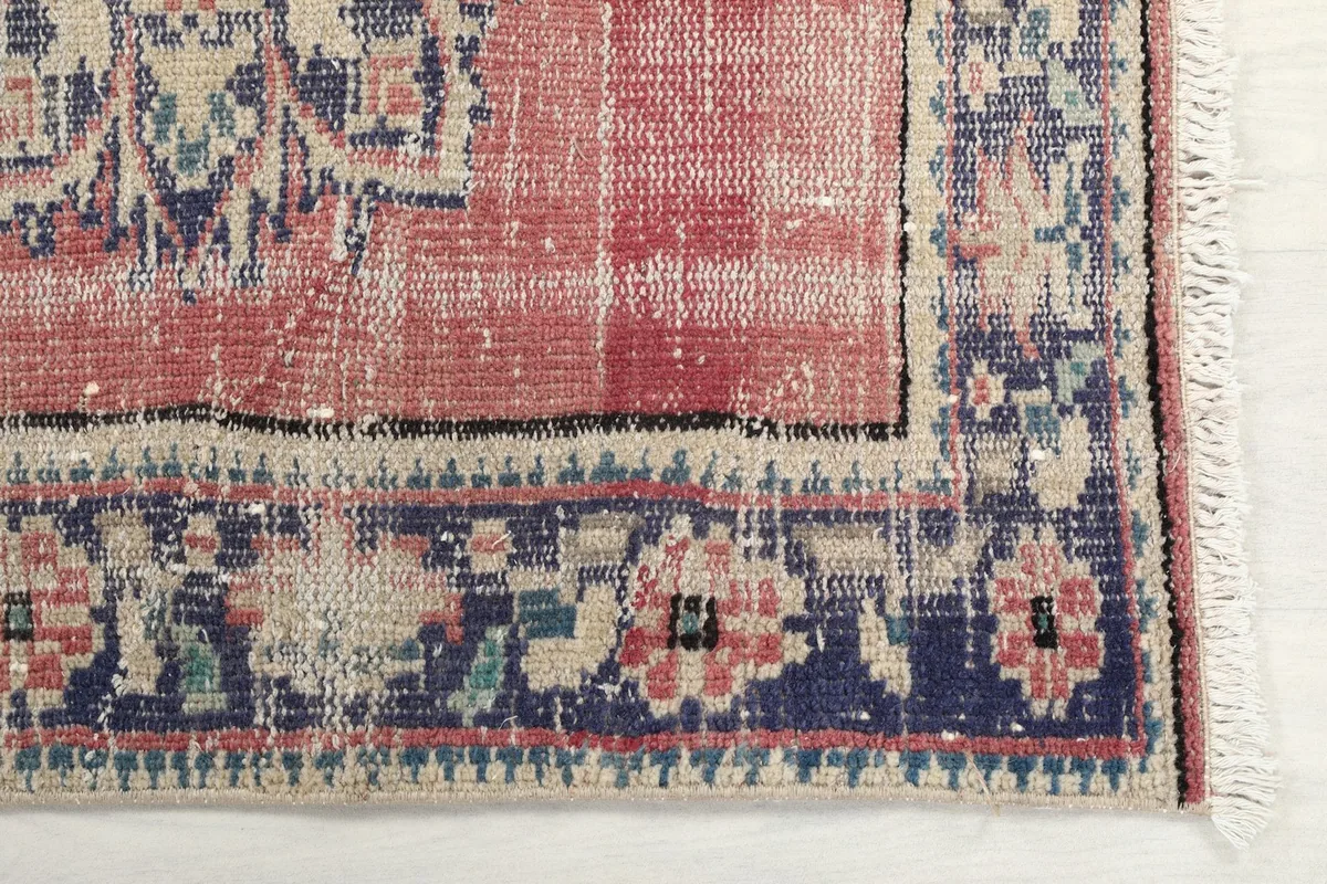 Detailed view of the navy border with floral motifs and the distressed rose field of the rug.