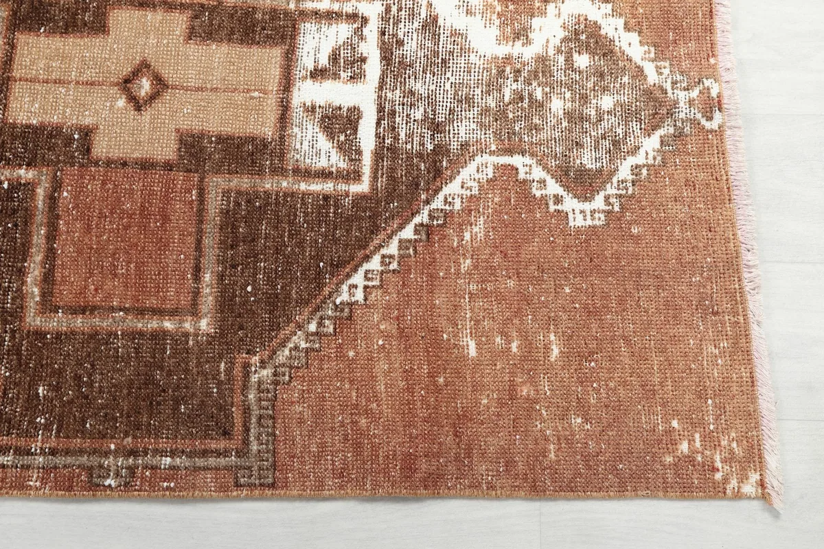 Detailed view of the rug's edge, showing the distressed rust field and the intricate border pattern.
