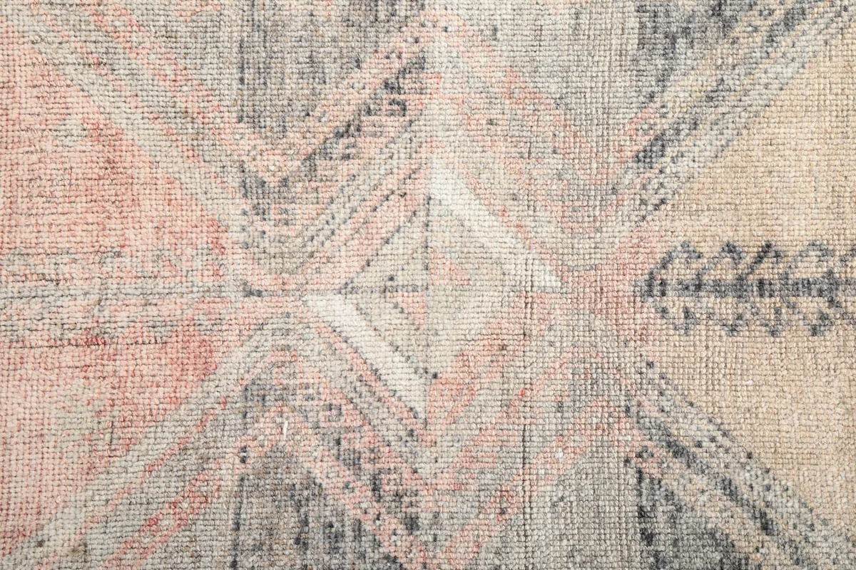 Close-up of the geometric pattern and faded wool pile texture in the rug's middle section