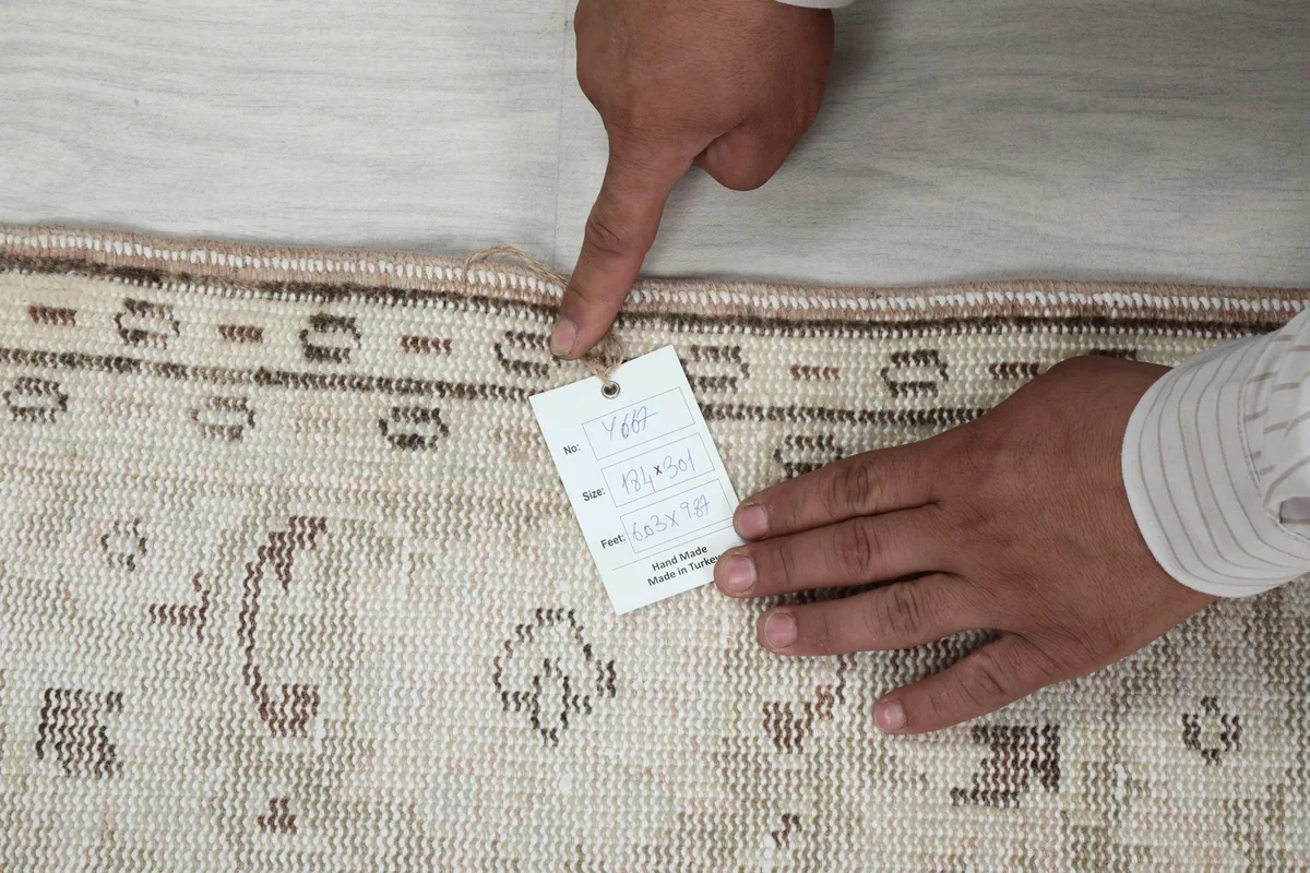 Hands pointing to the rug's edge and an attached product tag with size and origin information