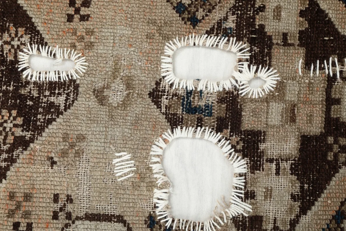 Close-up view of the low pile and areas where the cotton foundation is exposed due to wear.
