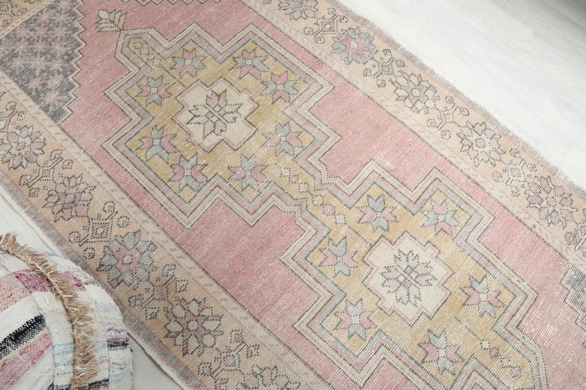 Overhead angled shot highlighting the central gold geometric design and pink field of the rug