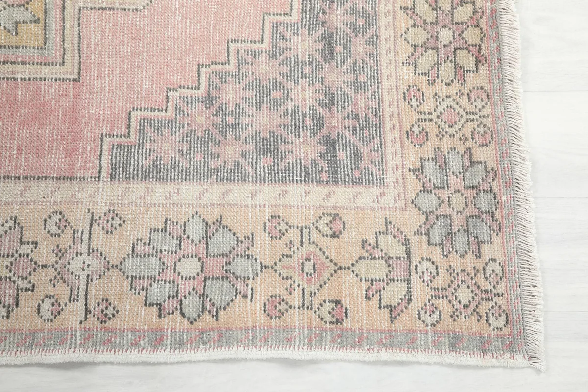 Detailed view of the corner of the rug, showing the beige border with floral motifs and gray accents