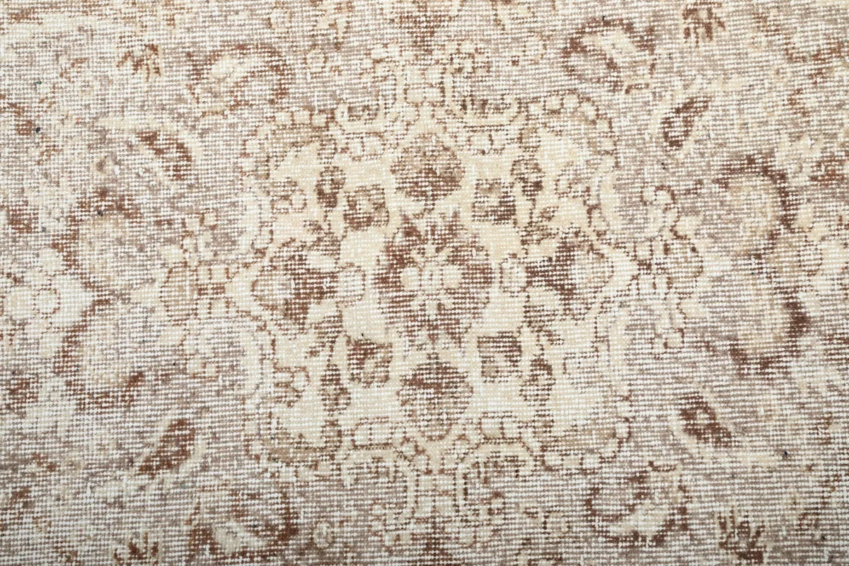 Close view of the low wool pile texture and faded tan patterns on an ivory background