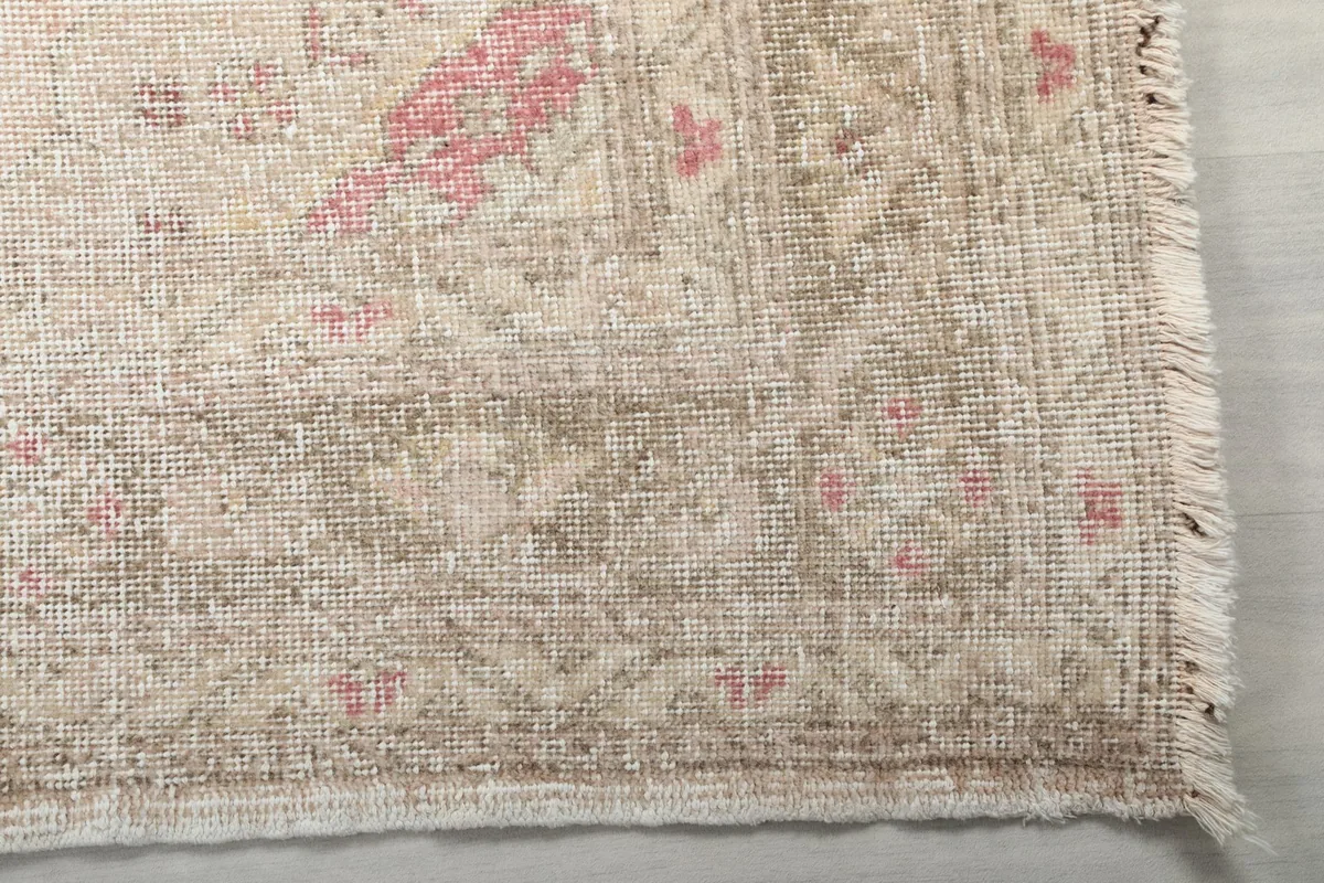 Detail of the rug's border and fringe, showing the faded rose and gray tones
