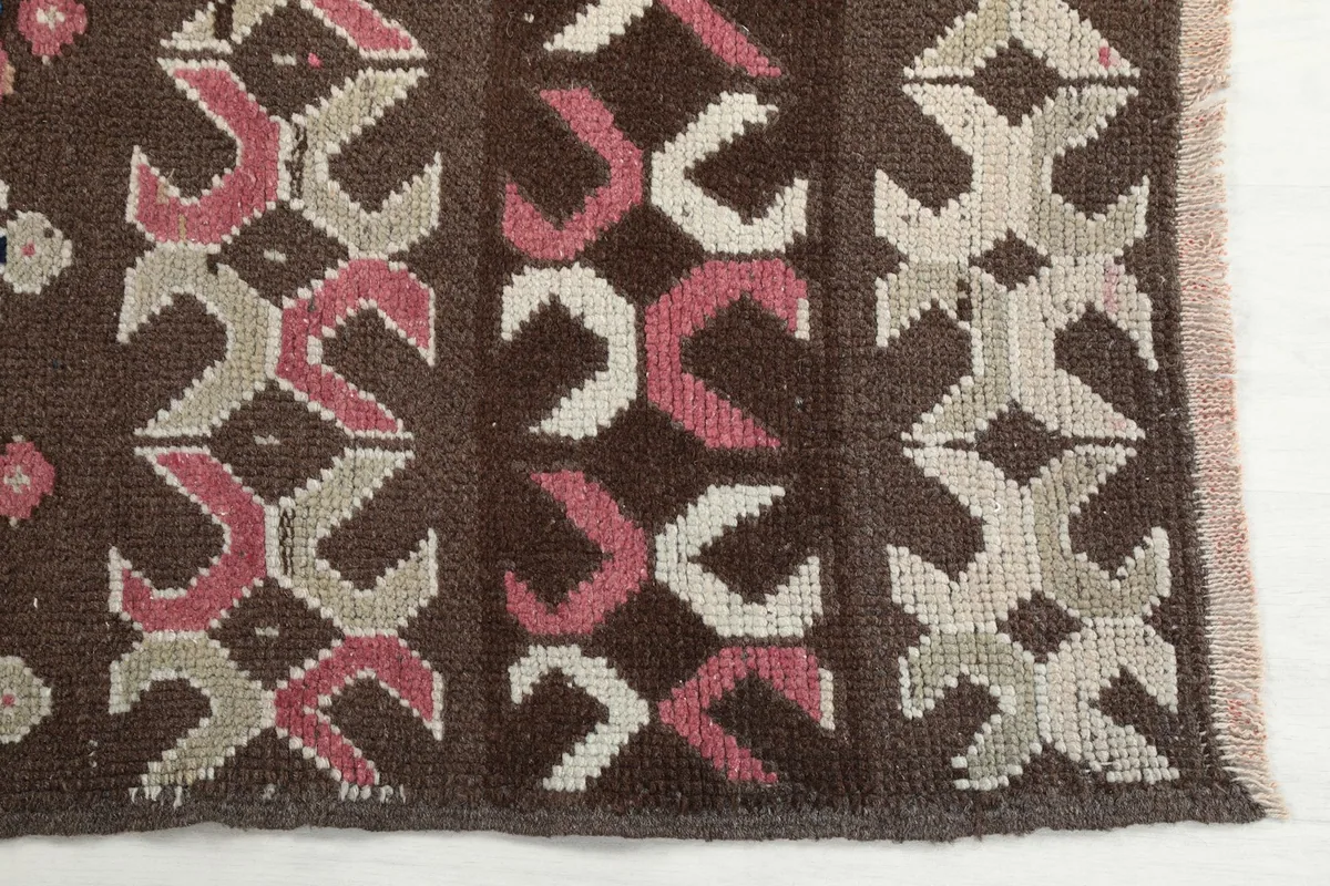 Detailed view of the brown field with pink and beige geometric motifs and the rug's edge.