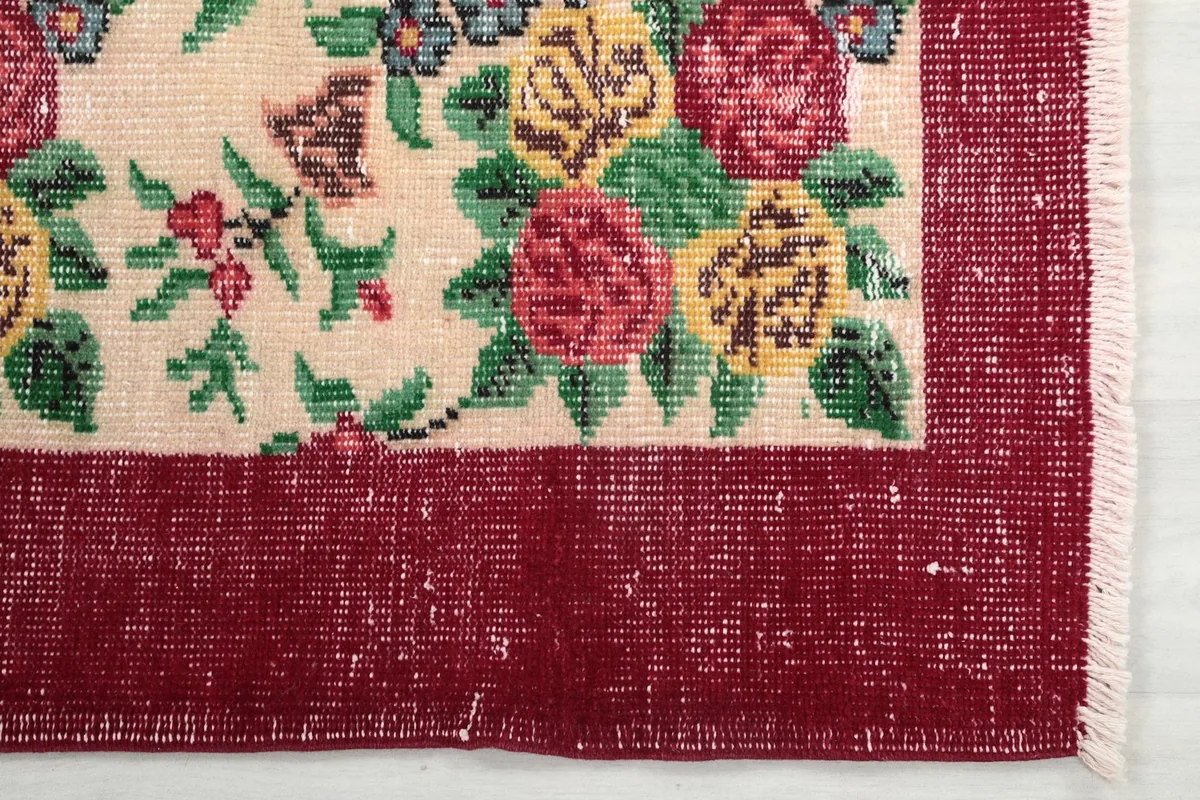 Detailed view of the red border and a corner of the cream field with floral motifs, showing light wear.
