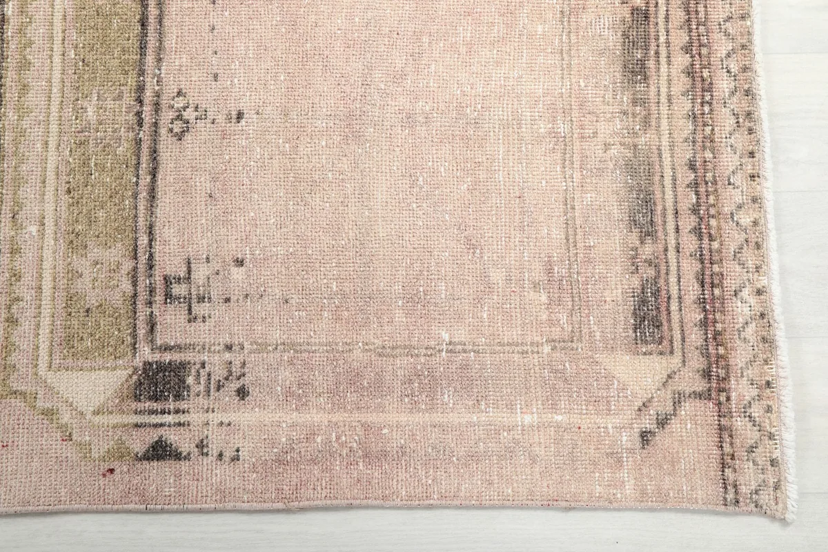 Detailed view of the distressed pink field and the intricate border design with brown accents on the runner.