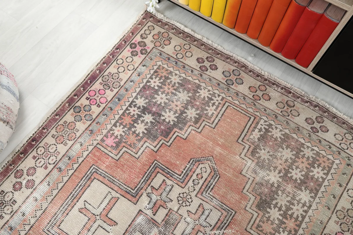 Top-down angle of the rug's end, revealing the intricate border and muted colors next to a bookshelf.