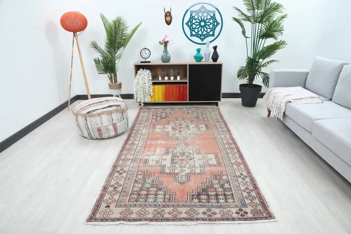 Vintage orange and beige geometric rug placed in a modern living room setting with a gray sofa and plants.