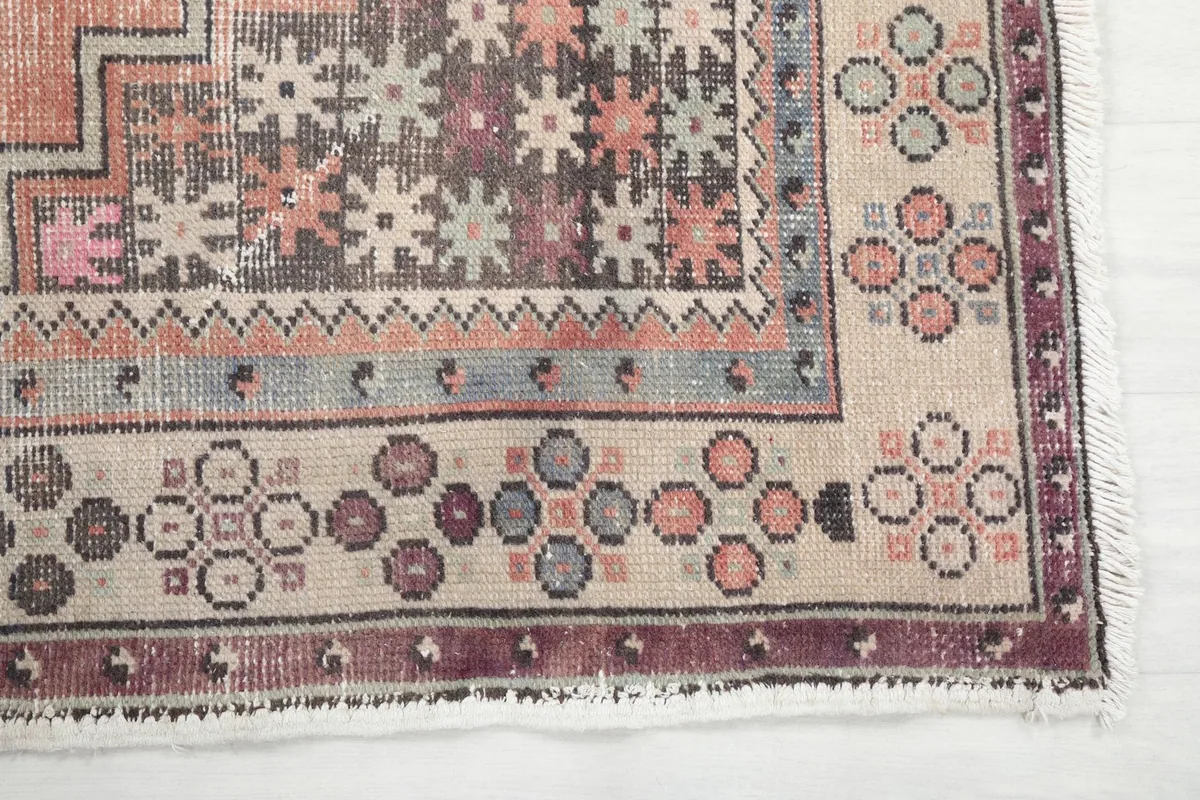Detailed corner view of the rug's border, showcasing the small circular patterns and faded colors.