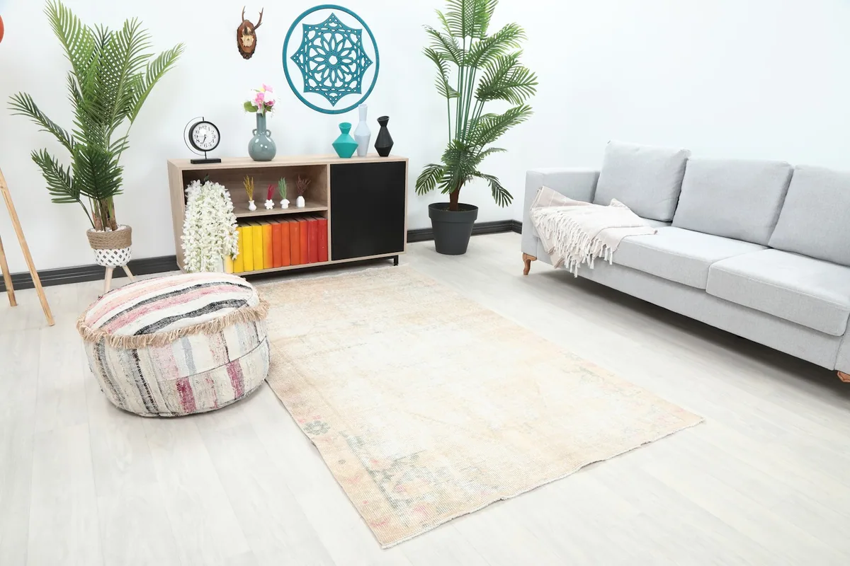Area rug in an ivory and rose geometric pattern, shown in a living room with a sofa and pouf.