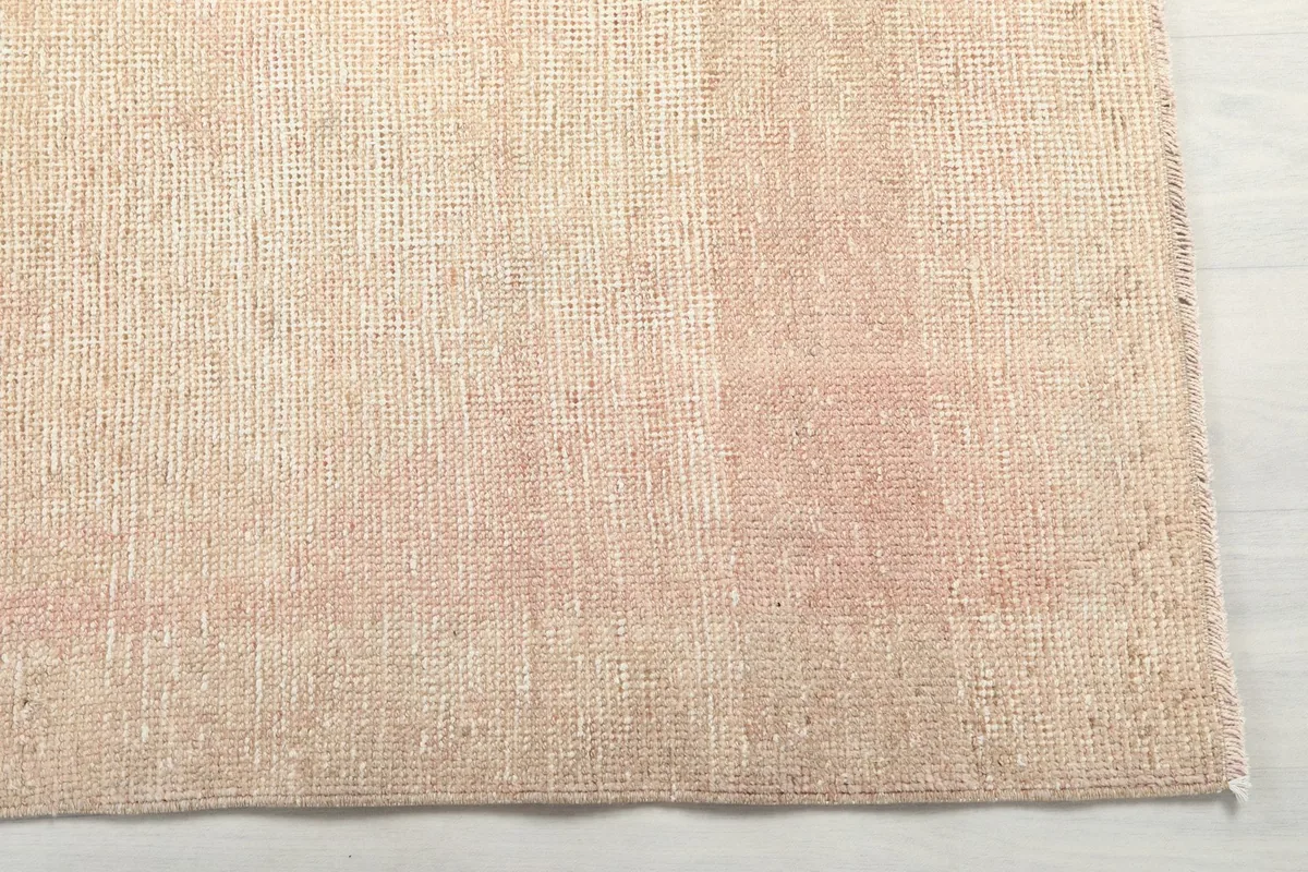 Close-up of the rug's surface, showing subtle rose tones and distressed texture in the beige pile.