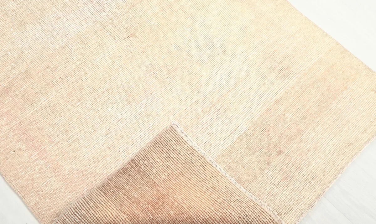 Corner of the rug folded back, revealing the tightly woven cotton foundation and short wool pile.