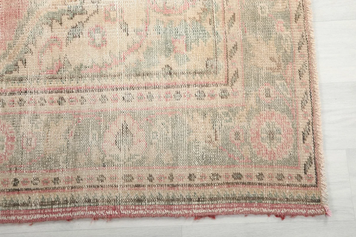Detailed view of the rug's border pattern, showing muted green and rose tones with fringe.
