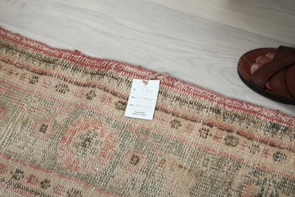 Detail of the rug's edge and fringe, with a product tag visible near a shoe for scale.