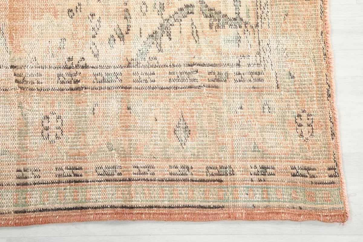 Close-up detail of the rug's corner, showing the muted orange color and geometric border pattern