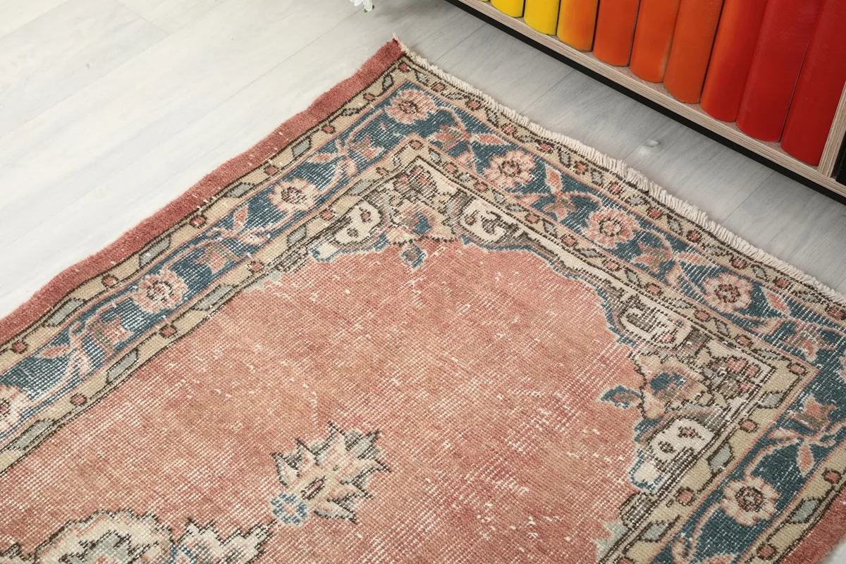 Angle view of one end of the runner rug, showing the border design and faded rust pile.