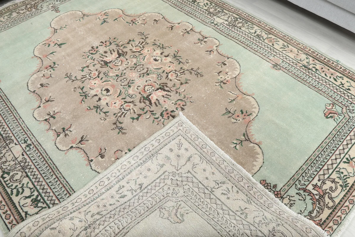 View of the Faded Green Floral Medallion Rug's front and a folded-back corner revealing the cotton foundation.