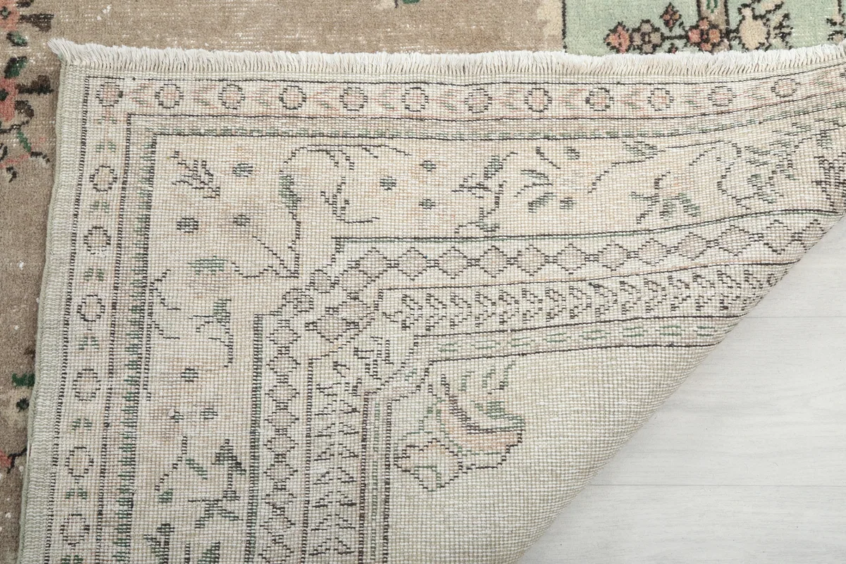 Close-up of the Faded Green Floral Medallion Rug's backing, showing the hand-knotted construction and fringe.
