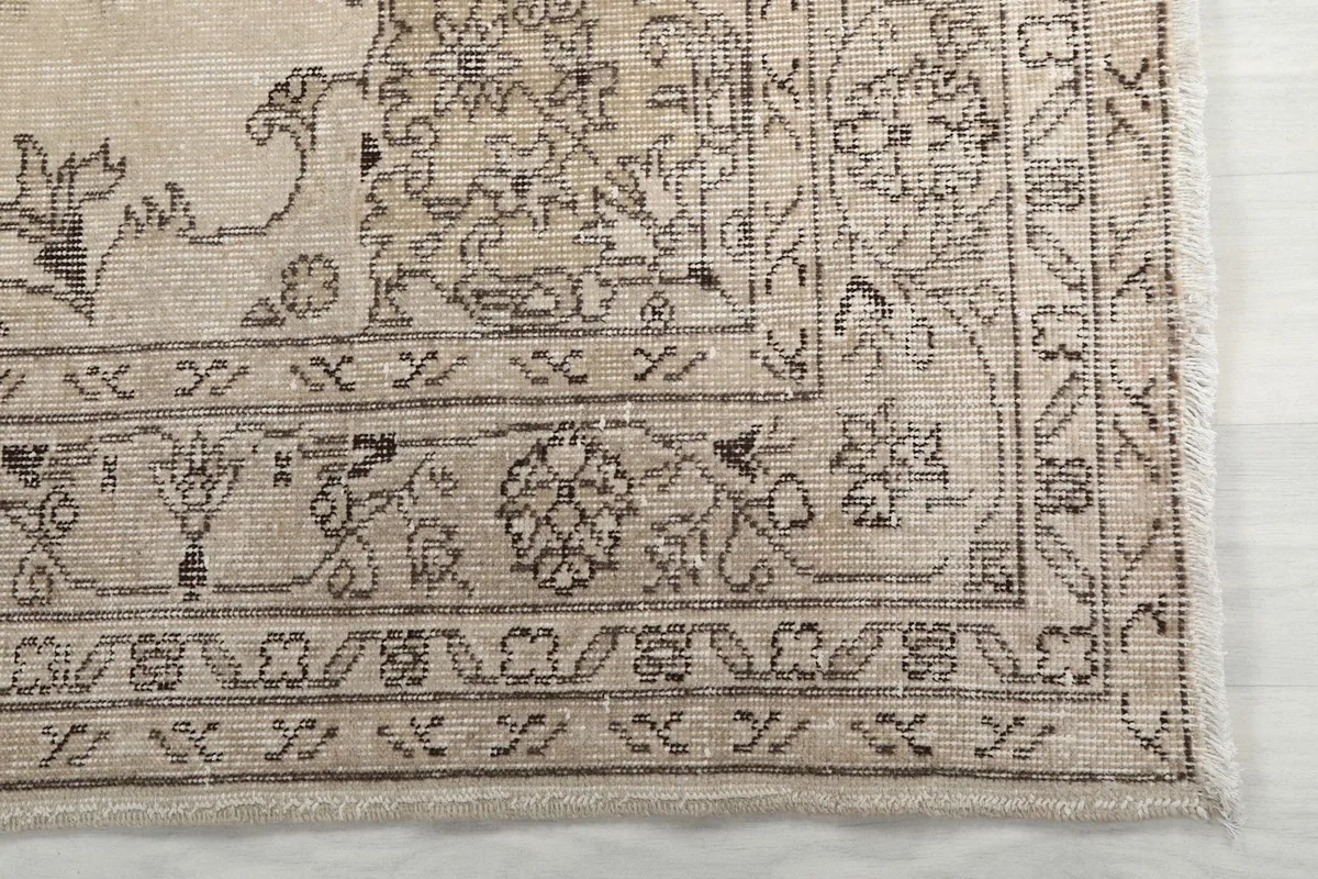 Detail of the rug's outer border pattern and a corner, showing the gray motifs on an ivory field.