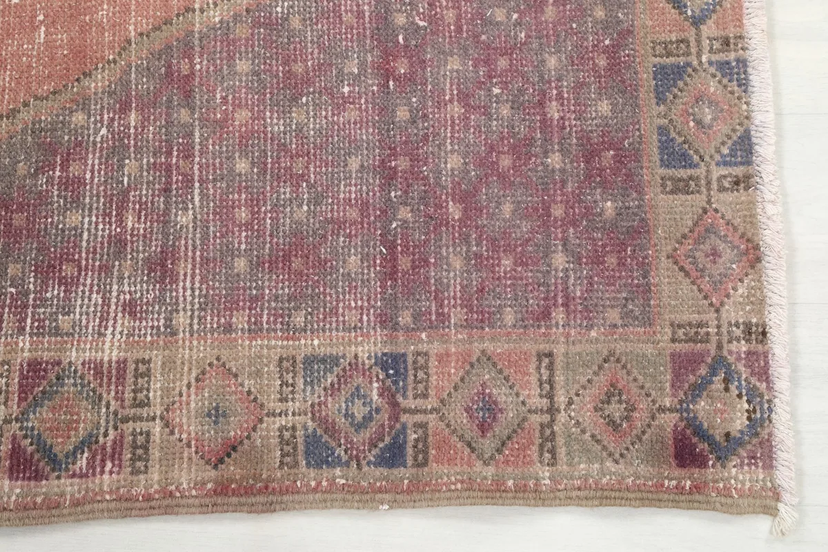 Detailed view of the rug's border pattern in beige, blue, and rose, showing hand-knotted texture