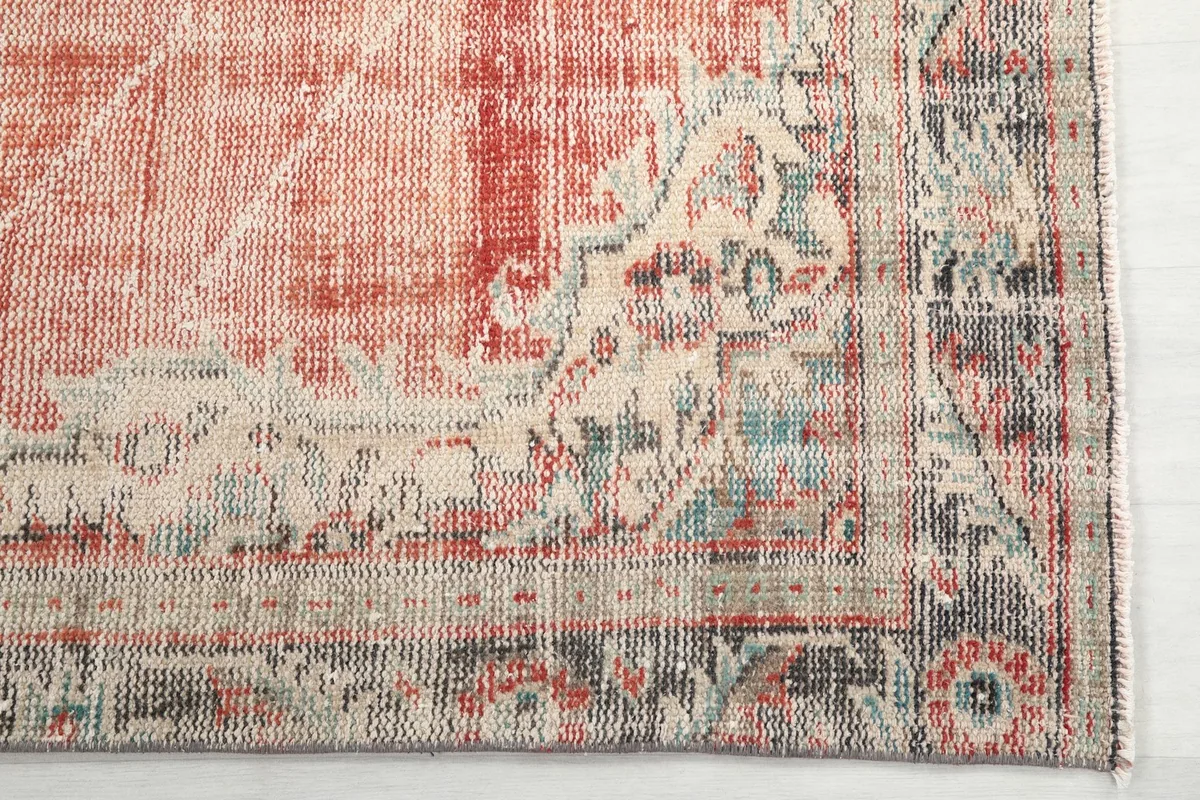 Detailed corner of the rug showing the beige and gray border patterns against the rust field.