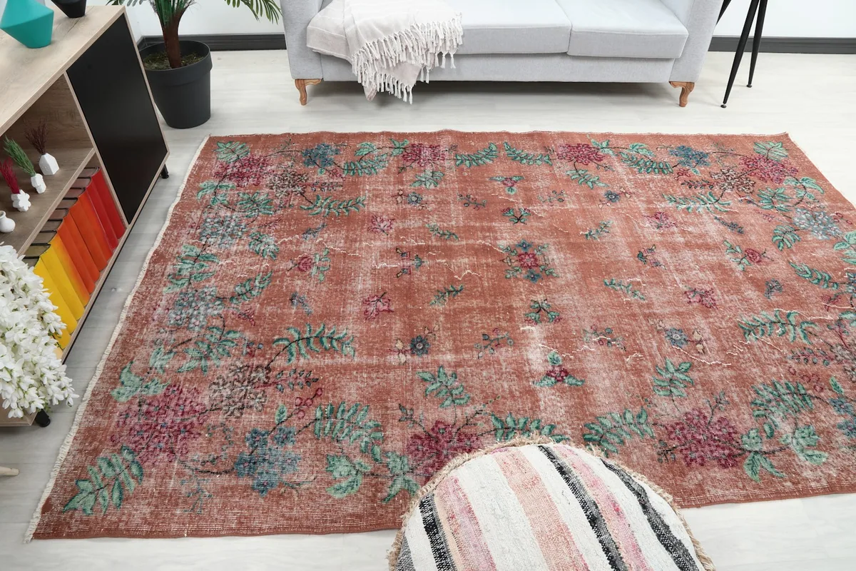 Full view of the rust floral rug in a room, showing its size relative to a sofa and ottoman