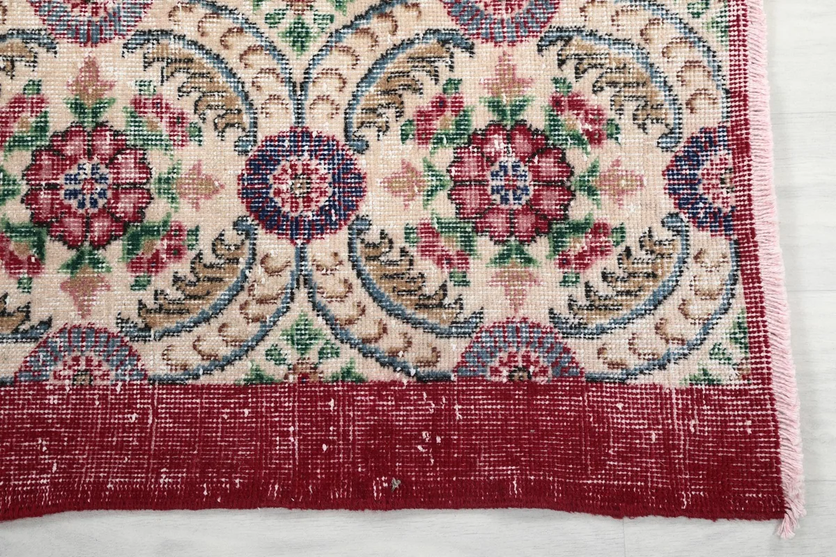Detailed view of the red border and a corner of the cream floral vintage rug