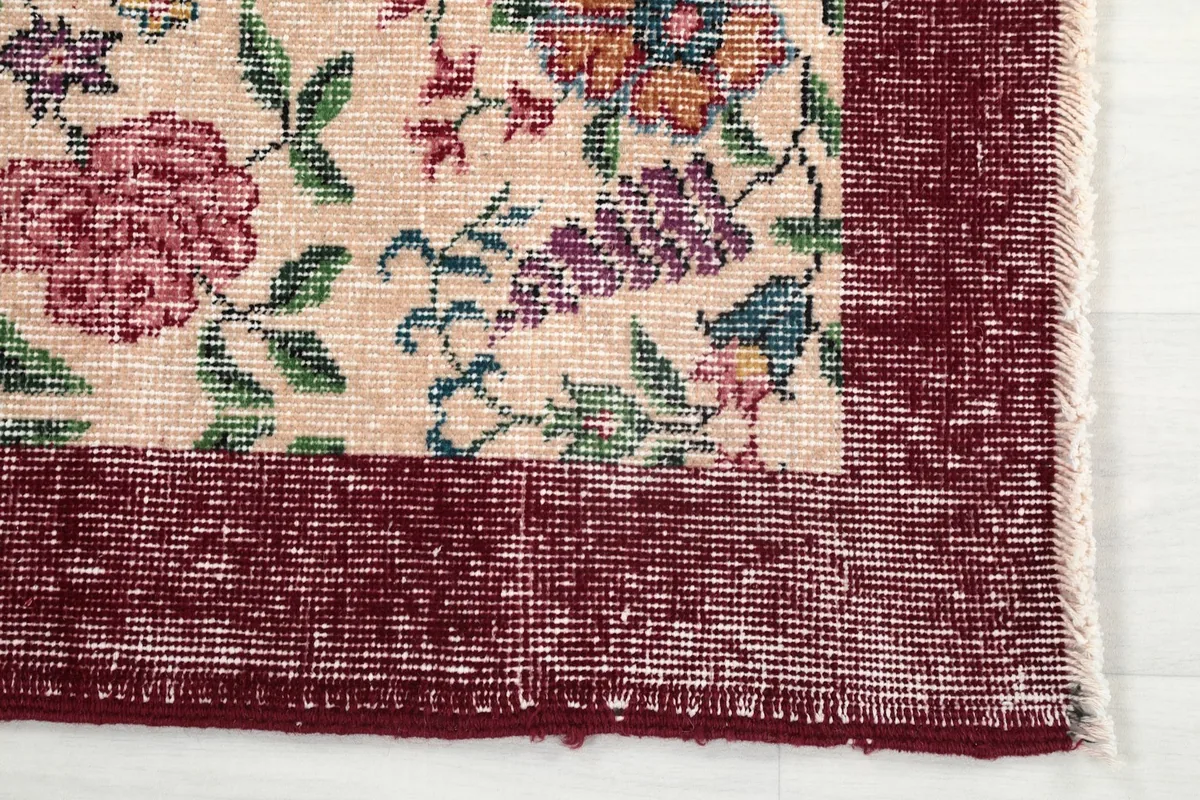 Detail of the rug's distressed red border and beige field with floral elements.