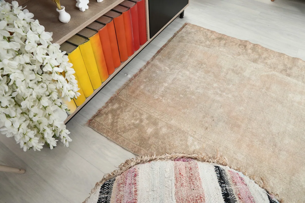 Diagonal view of the beige rug, showing the blend of colors and the worn areas