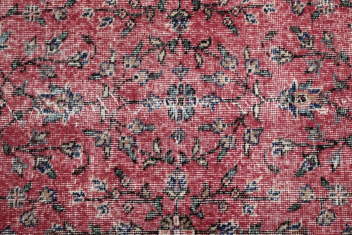 Extreme close-up of the rug's rose pile, showing individual knots and subtle wear in the floral motifs
