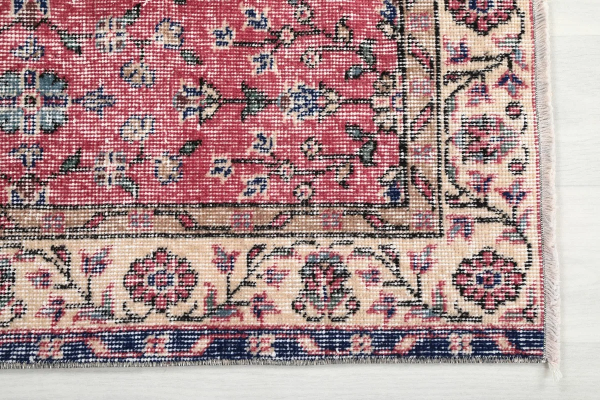 Detailed view of the corner of the rug, highlighting the beige border with floral patterns and navy edge