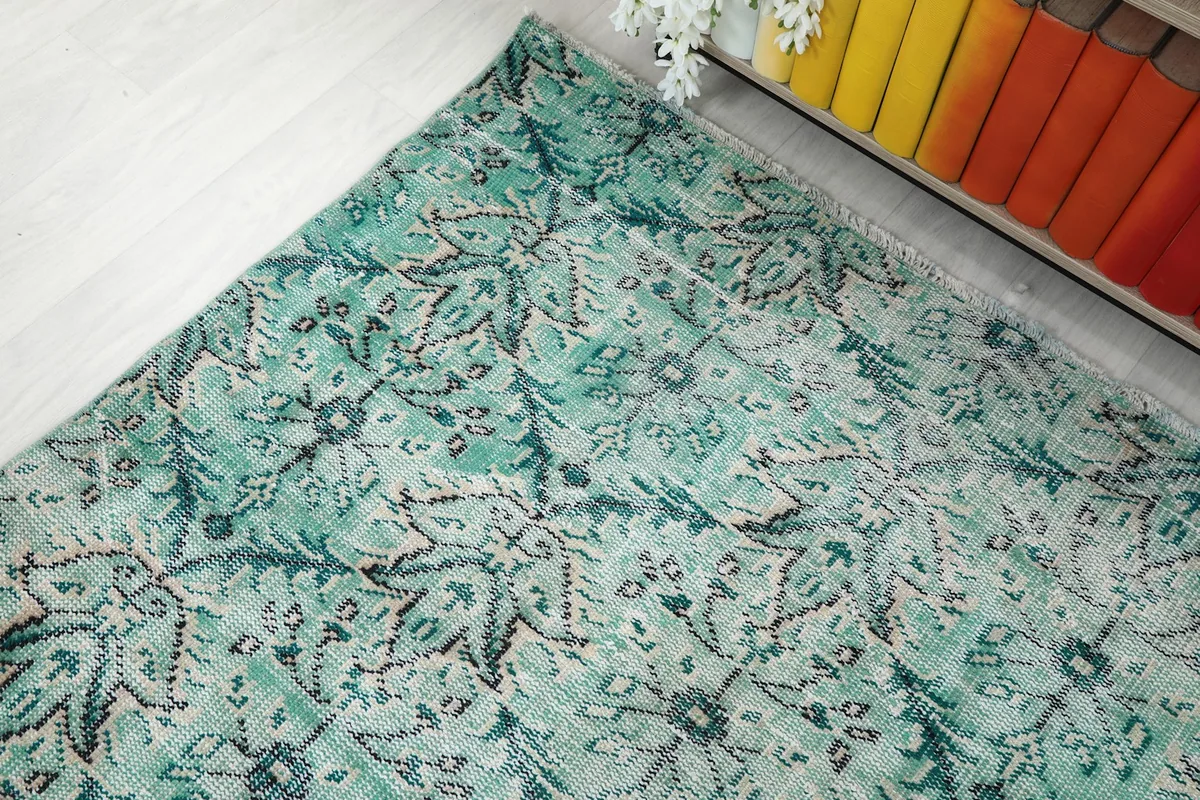 Corner view of the rug with its green and blue patterns extending towards a shelf