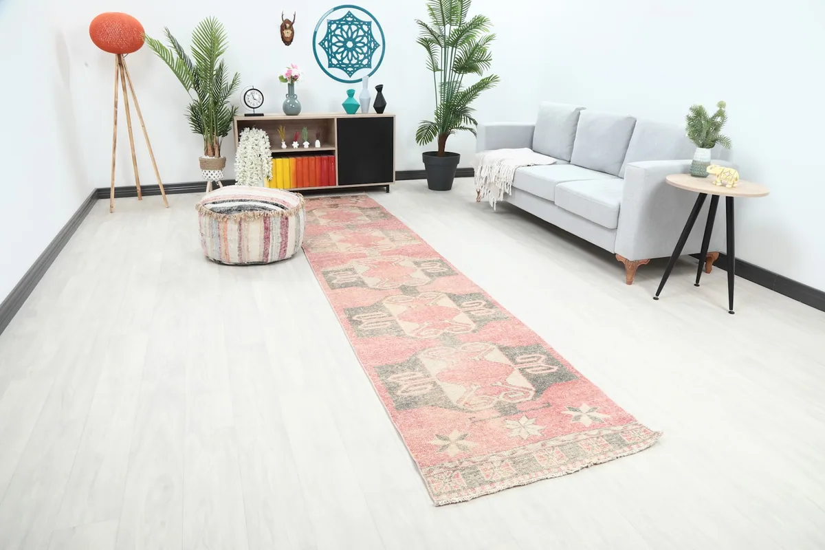 Overall view of the rose and gray geometric runner in a bright room setting with a sofa and pouf.