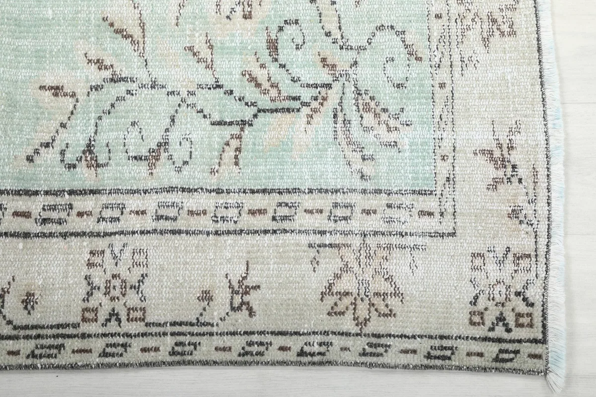 Detailed view of the corner border pattern and faded green field of the rug